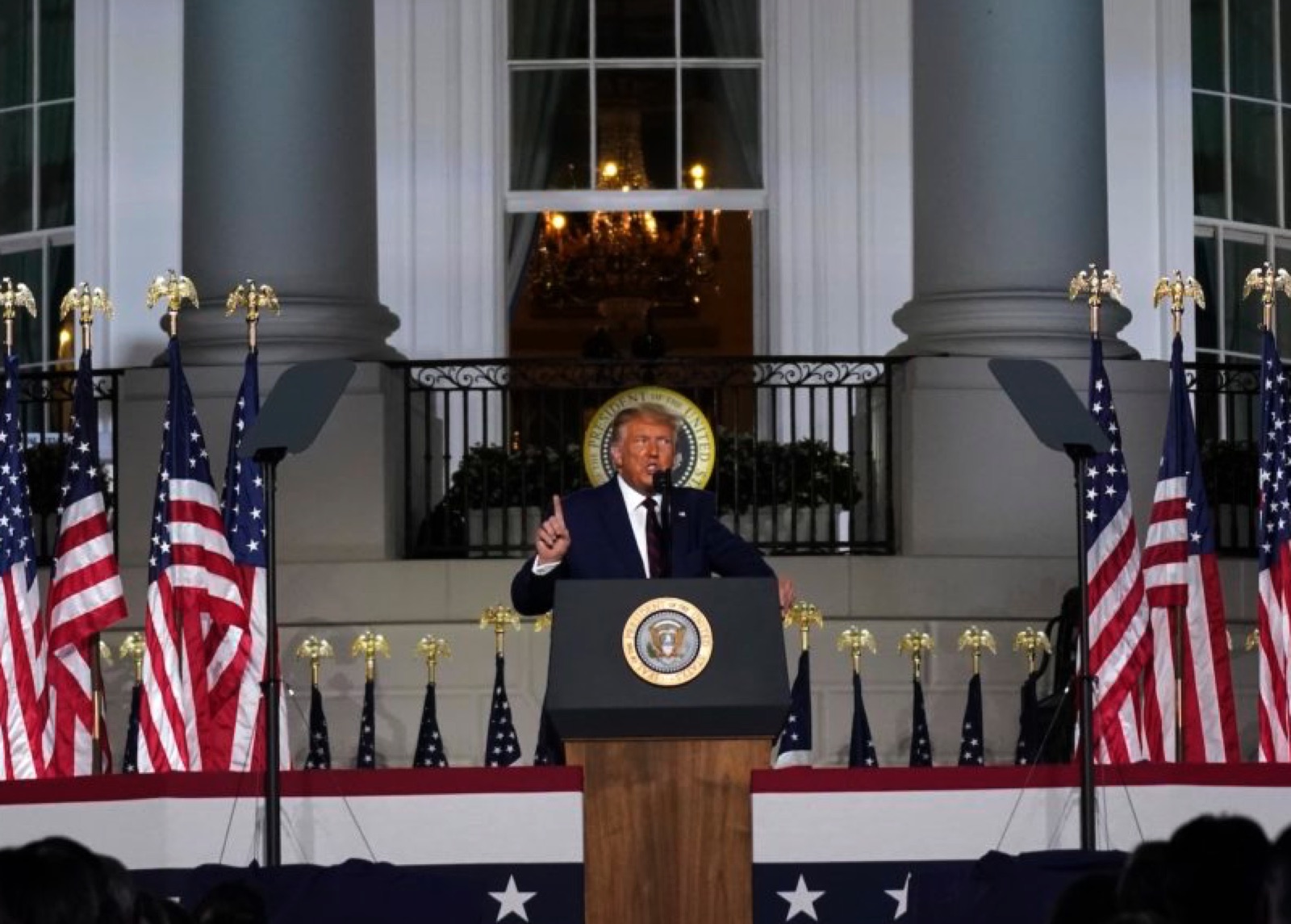 President Trump delivering an address at the White House, flanked by American flags